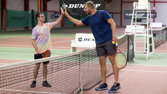 Ein Athlet mit Beeinträchtigung und ein Athlet ohne Beeinträchtigung schlagen nach dem Tennisspiel die Hände zusammen